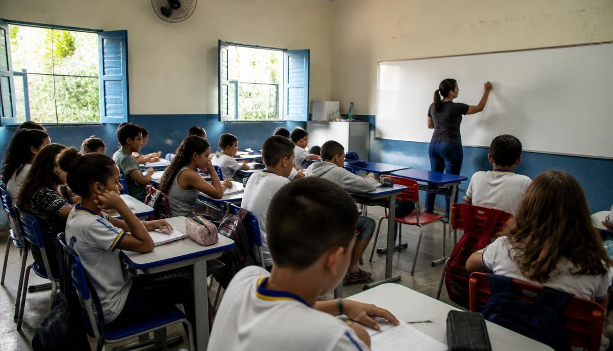 Sala de aula de escola pública em cidade do interior paulista, com alunos estudando e professora no quadro