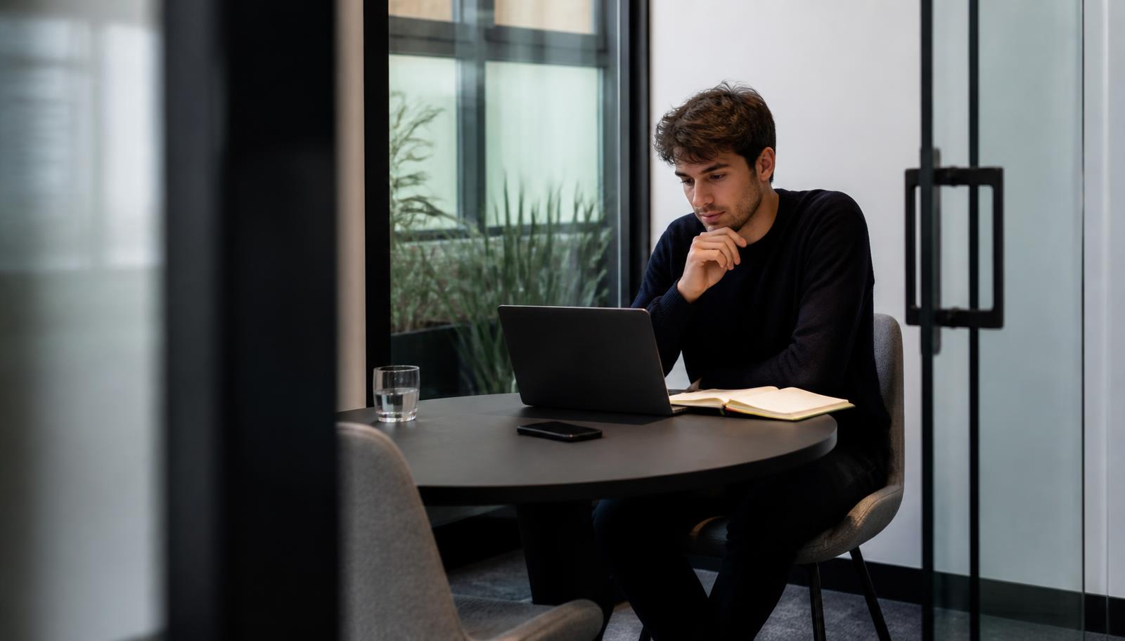 Empreendedor trabalhando com notebook em sala privativa de coworking, com parede de vidro e interior moderno